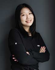 Kayla - Smiling woman with arms crossed against gray wall