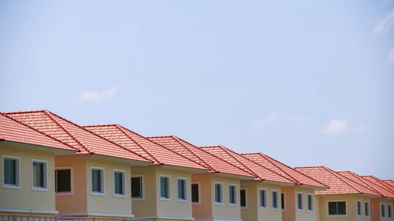 Row of light coloured apartment buildings with terracotta tile roofs under blue sky