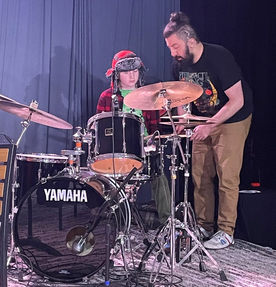 Young jazz drummer with an adult instructor on stage at Madison Jazz Society event, demonstrating jazz music performance and skill.