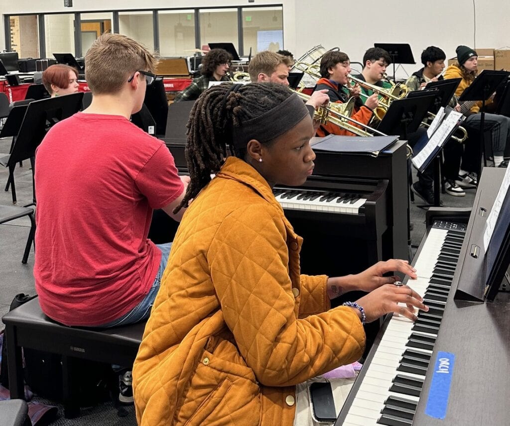 Students play electric keyboards side by side in a school keyboard lab