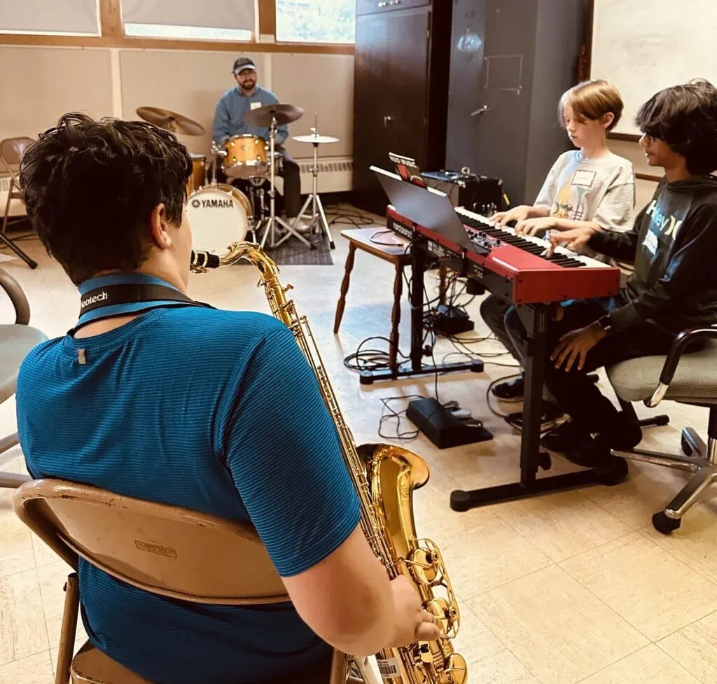 A saxophonist watches as a combo rehearses with drums and keyboards at iGnitE jAzz! 2026