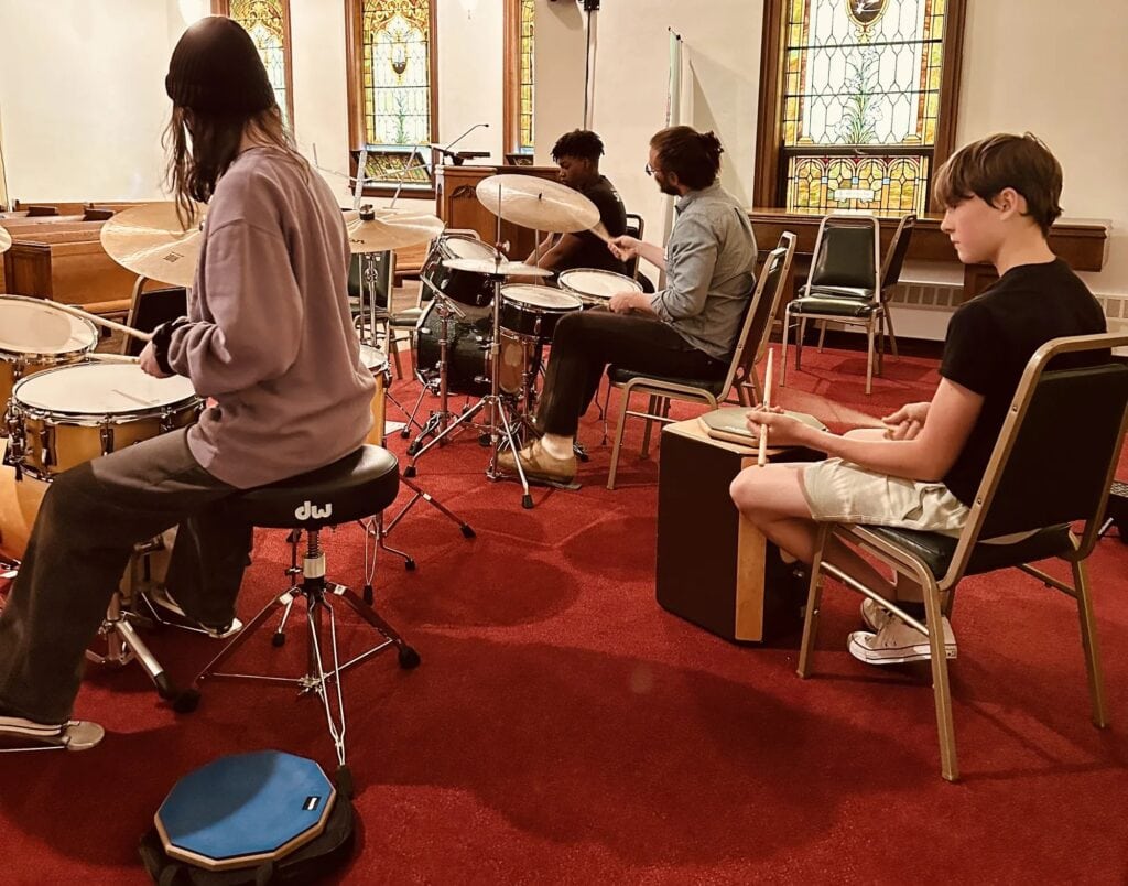 A small combo rehearses with a drummer and a student on cajon at iGnitE jAzz! 2026