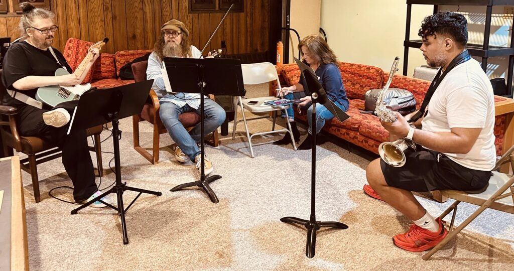 Guitar, violin, and saxophone players read music in a small-group rehearsal at iGnitE jAzz! 2026