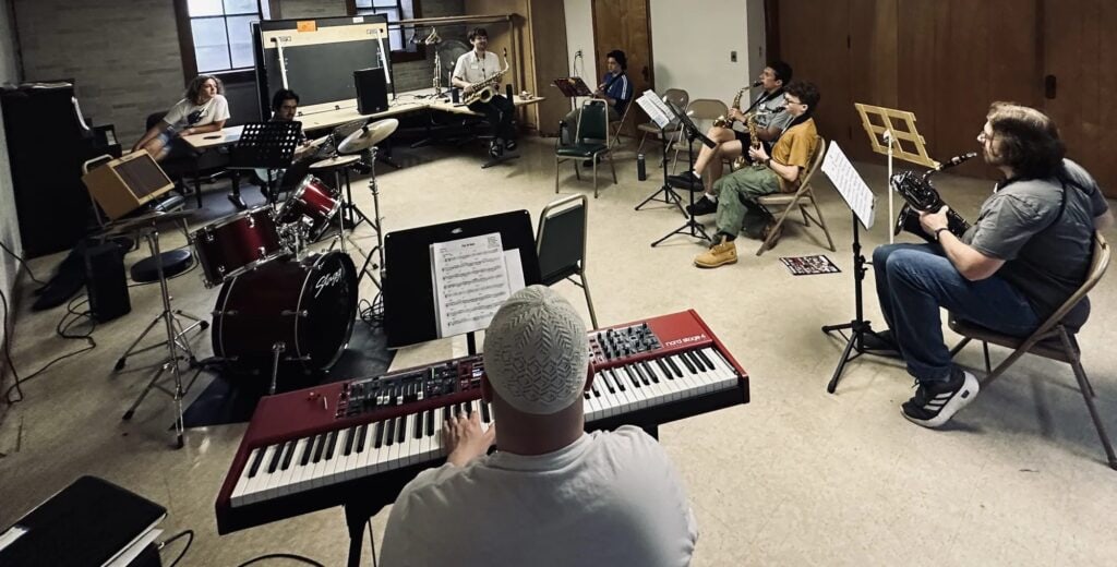 A keyboard player leads a rehearsal room of guitarists and horn players at iGnitE jAzz! 2026