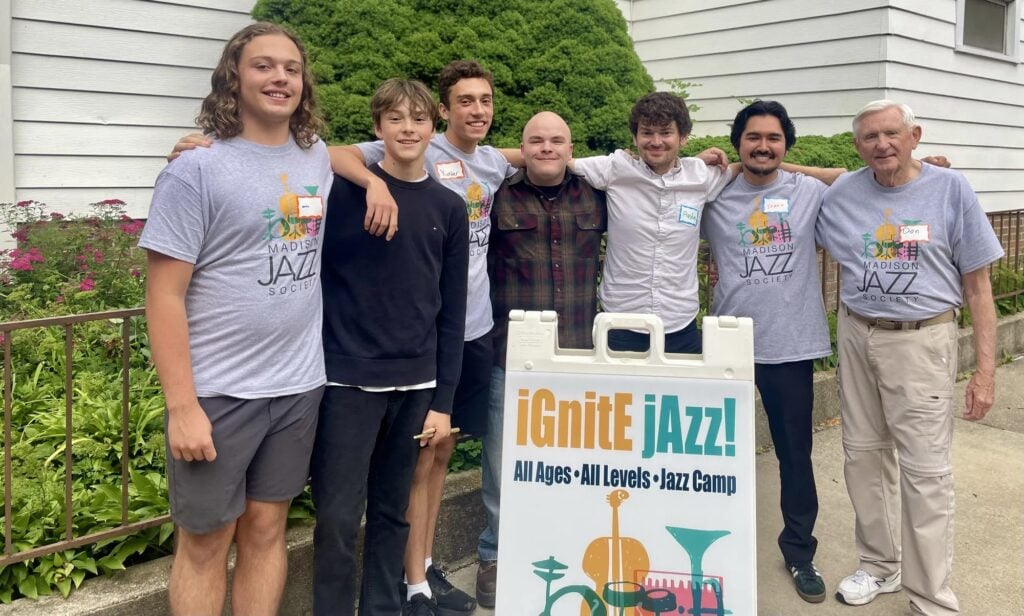 iGnitE jAzz! campers and instructors in camp t-shirts outdoors by the banner