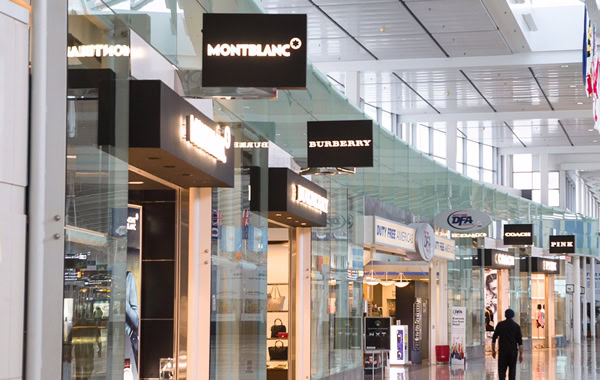 Luxury brand stores in a modern shopping mall with glass walls and signage.
