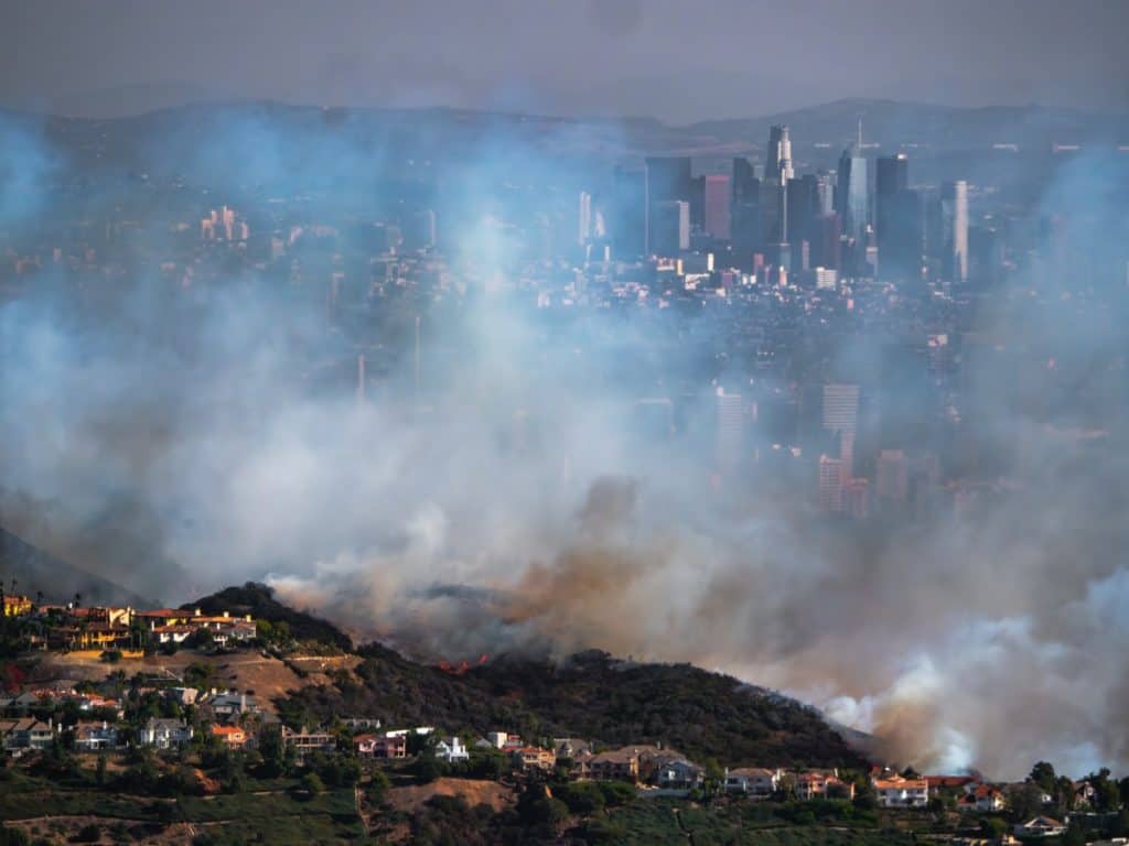 Thick smoke from a Los Angeles wildfire spreads toward residential neighborhoods and urban buildings, emphasizing the widespread impact that can lead to smoke damage claims for property and air quality losses.