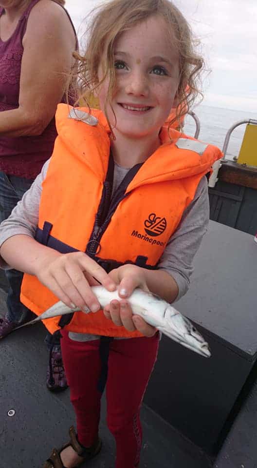 Young girl holding a fish on a fishing trip in Moray Firth.