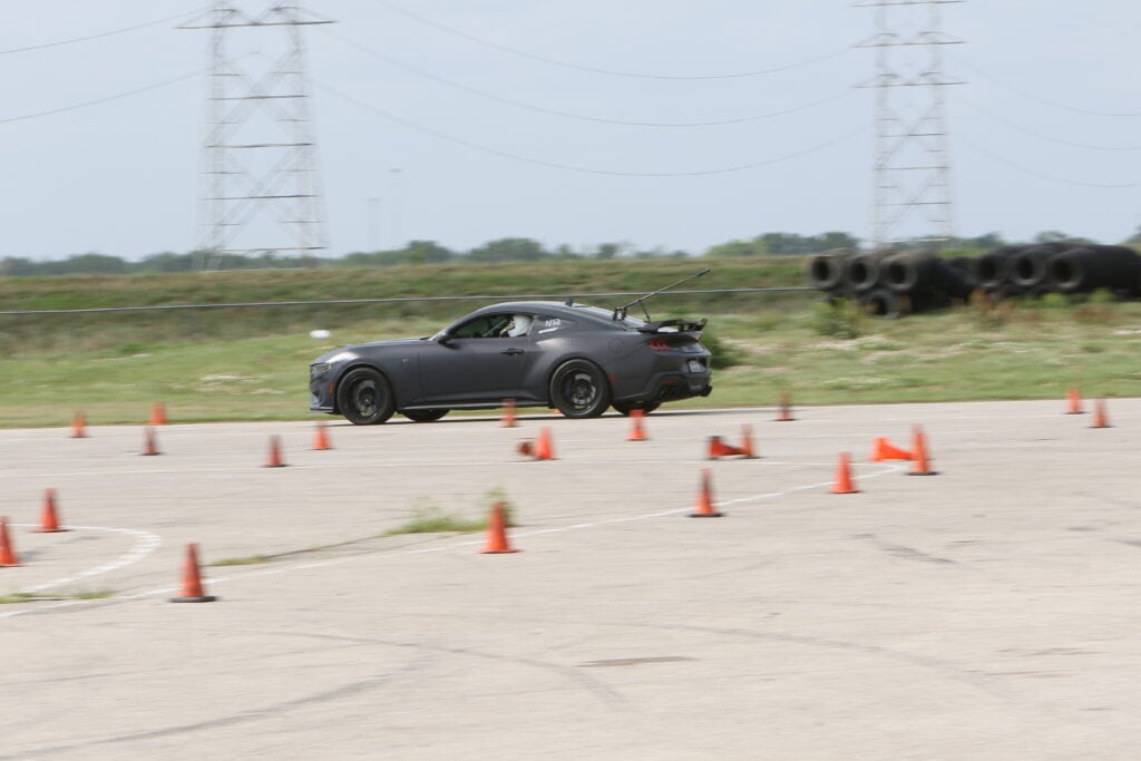 Black sports car navigating through autocross cones at Mustang Week 2026.
