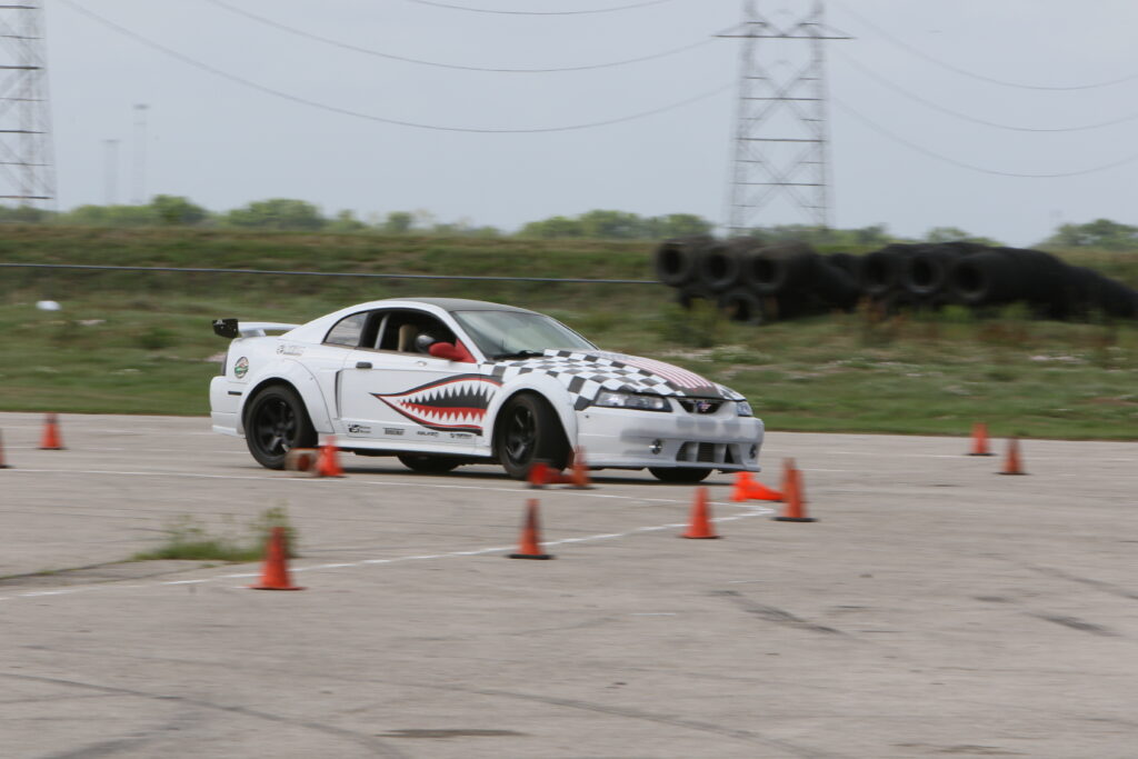 White Ford Mustang with shark graphic on side during autocross event.