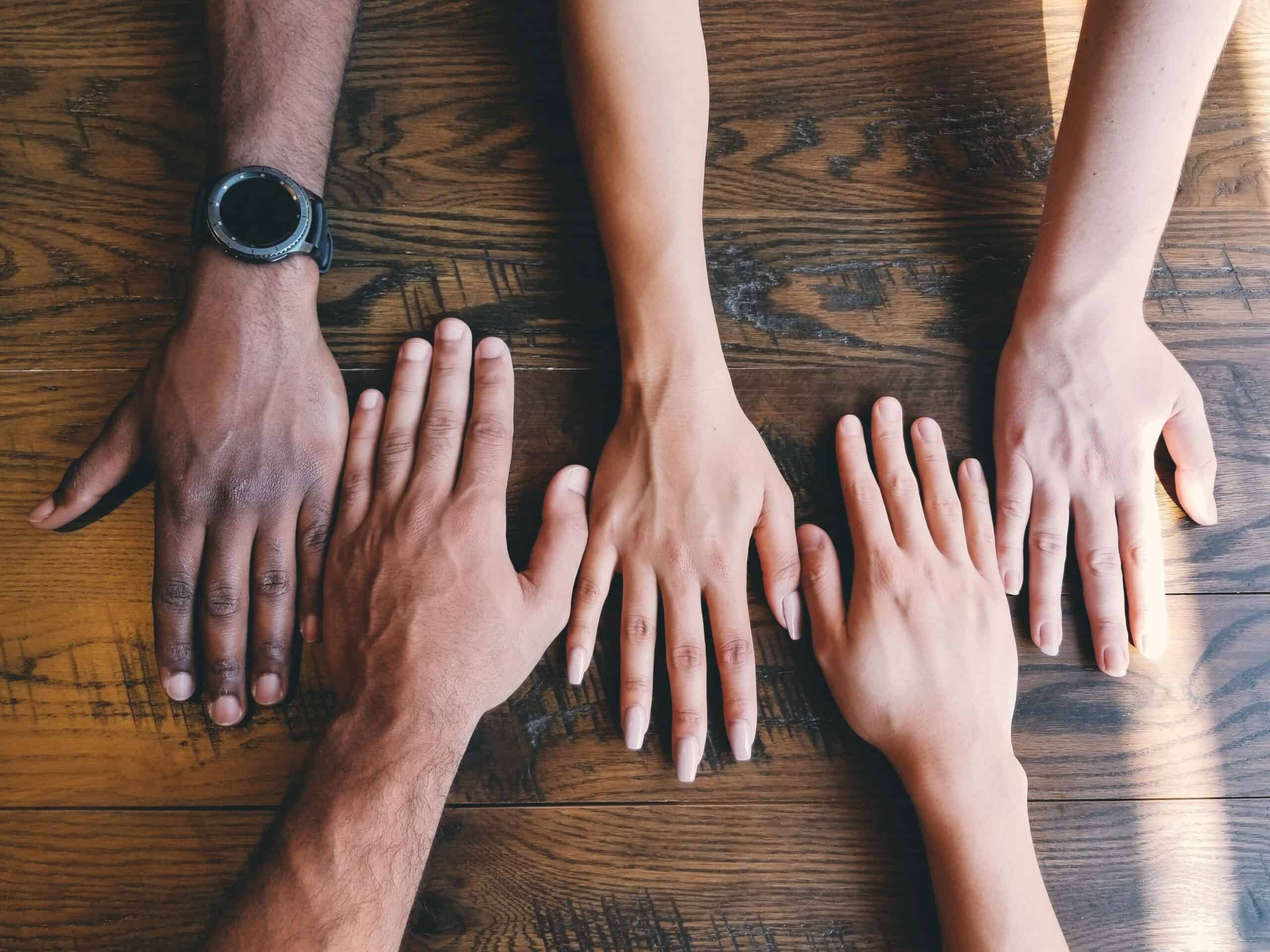 Diverse hands placed together on wooden floor for community support.