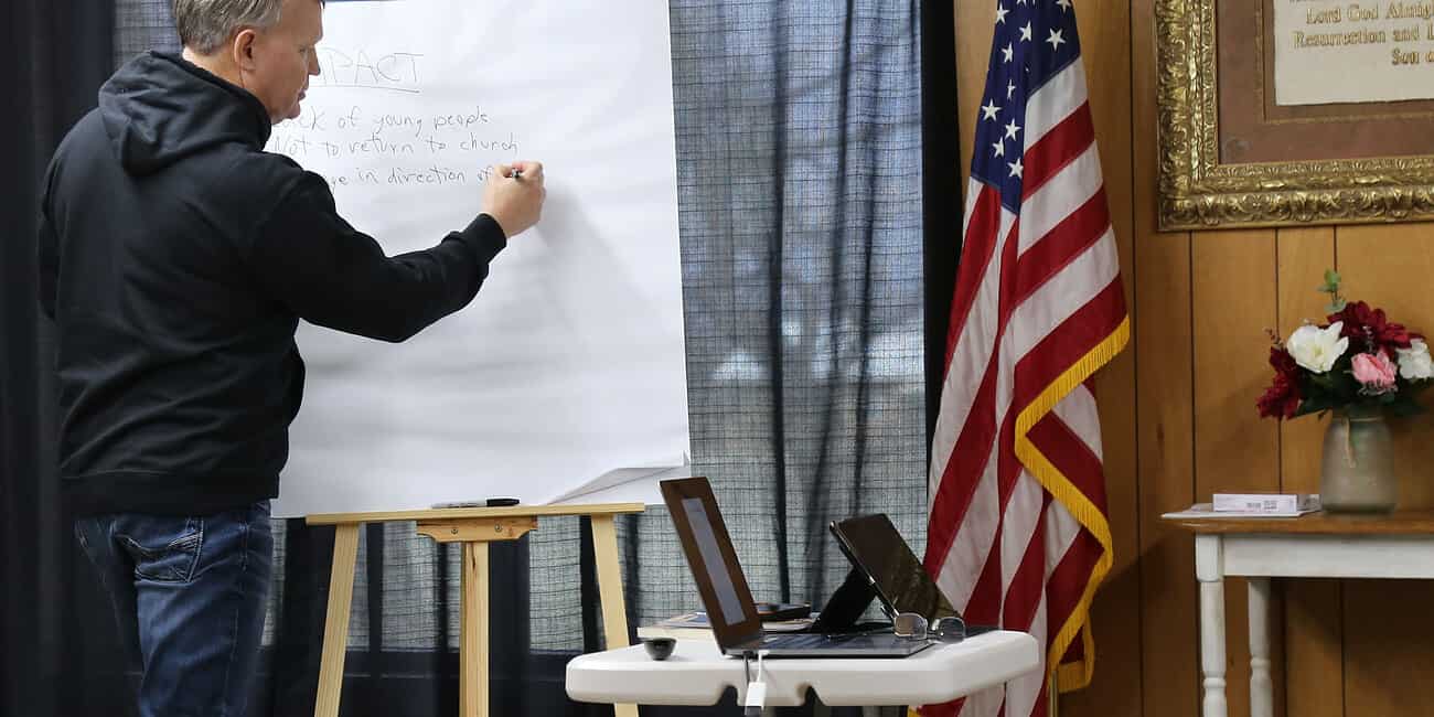Church leader writing on whiteboard during training session at NLW International event.