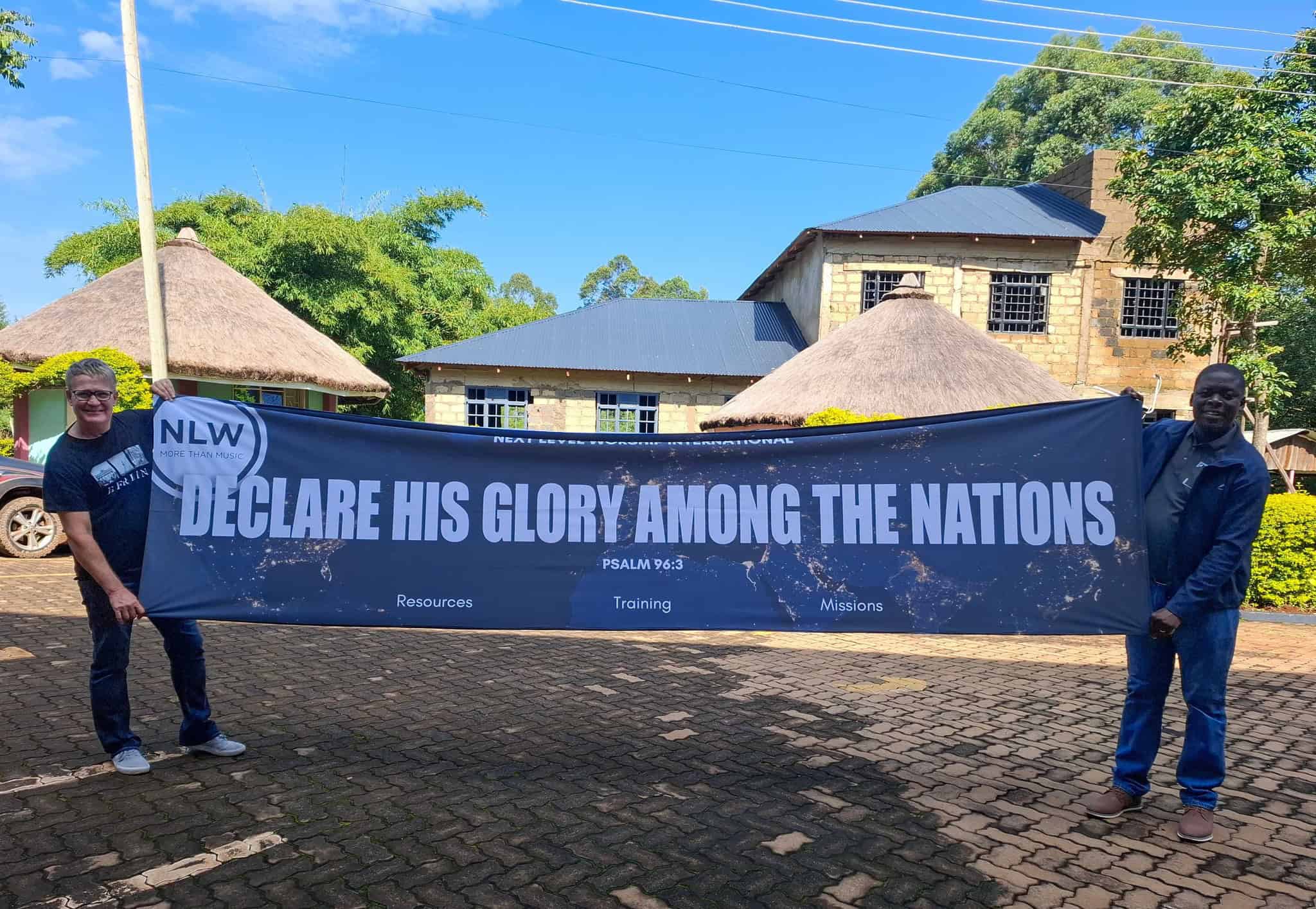 Two men holding a NLW International banner with the message "Declare His Glory Among the Nations" ou.