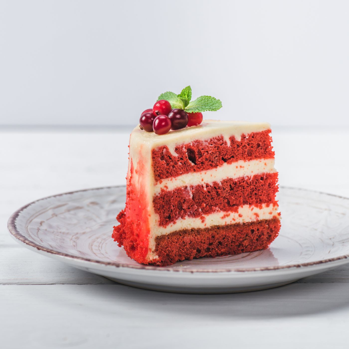 A slice of moist red velvet cake made with box cake mix and pudding, layered with creamy frosting and topped with fresh cranberries and mint. This easy, bakery-quality cake has a soft, fluffy texture thanks to the instant pudding mix hack, making it a perfect dessert for any occasion.