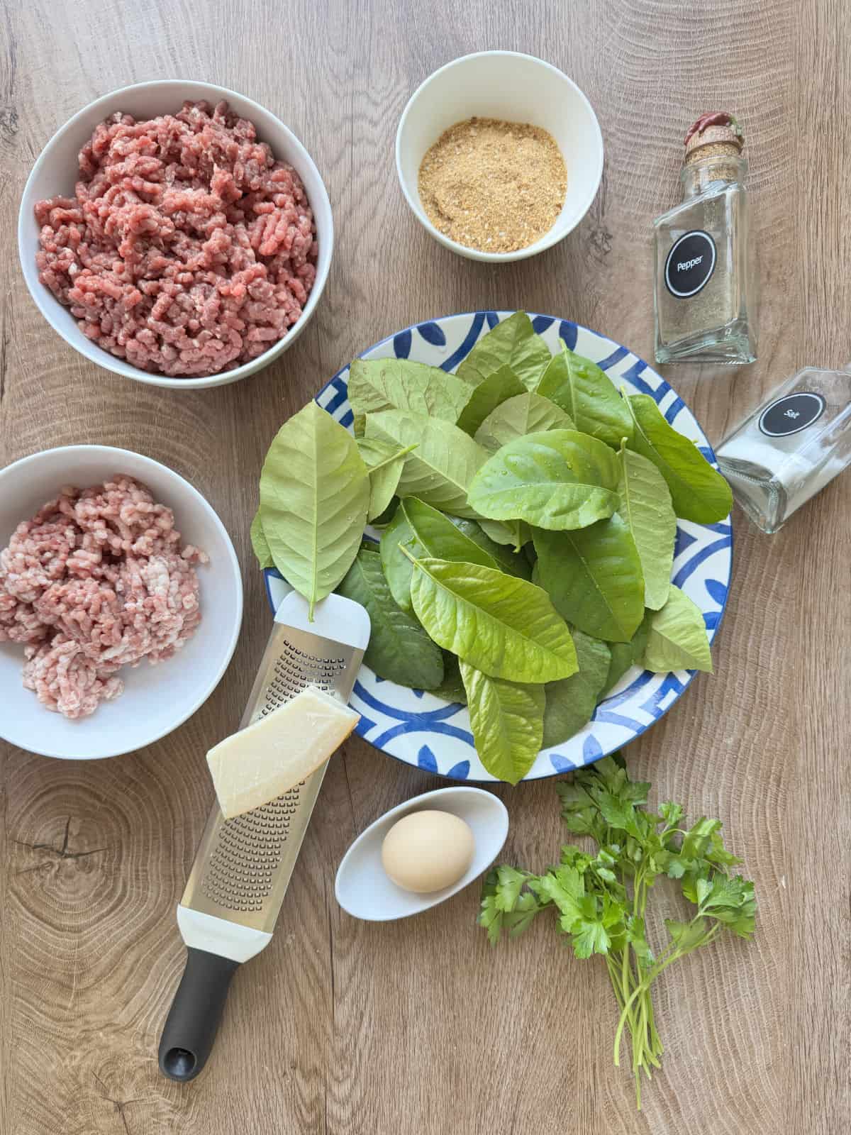 Ground beef, herbs, spices, cheese, egg, and seasoning on a wooden table for cooking.
