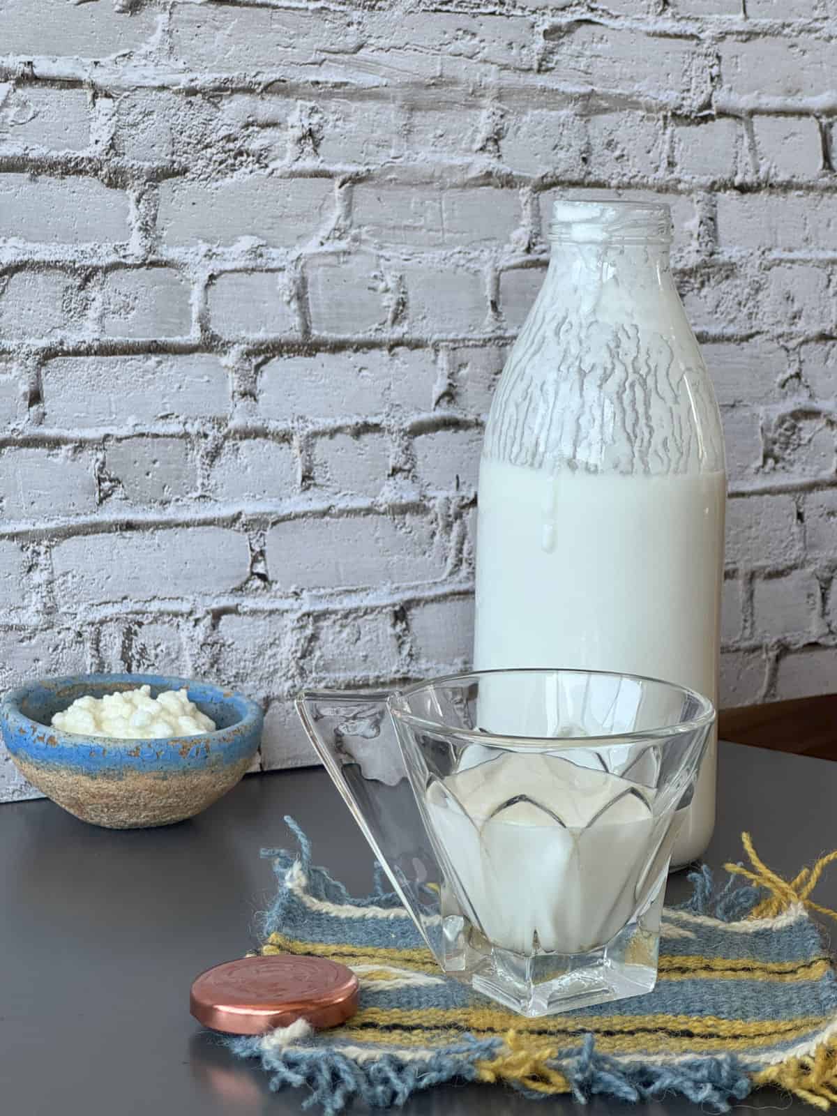 Bottle of kefir with a glass and kefir grains in a background.