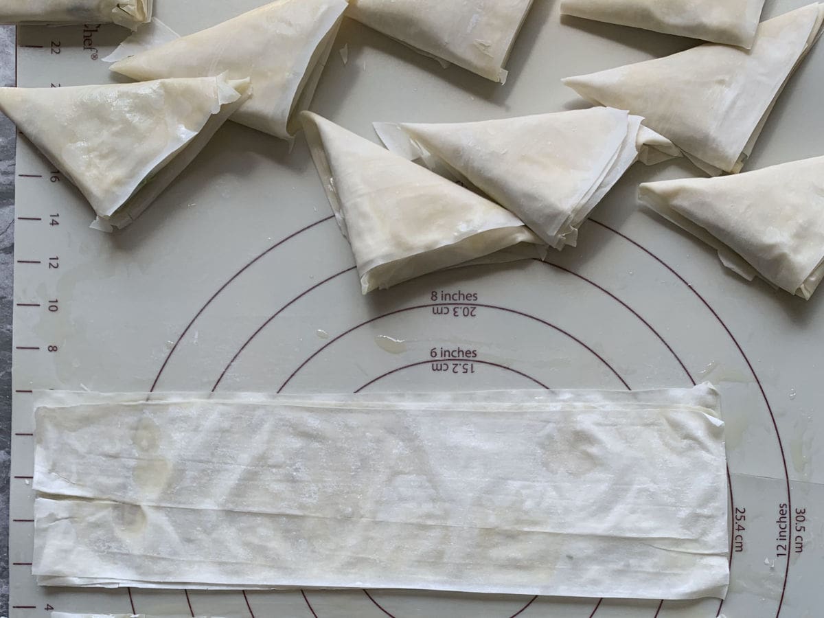 Ready spanakopita triangles on a work surface.