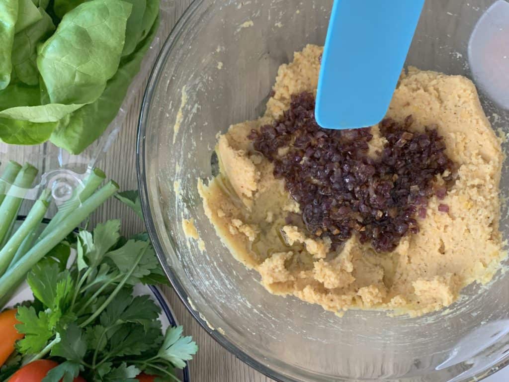 Adding fried onions to lentil bulgur mixture.