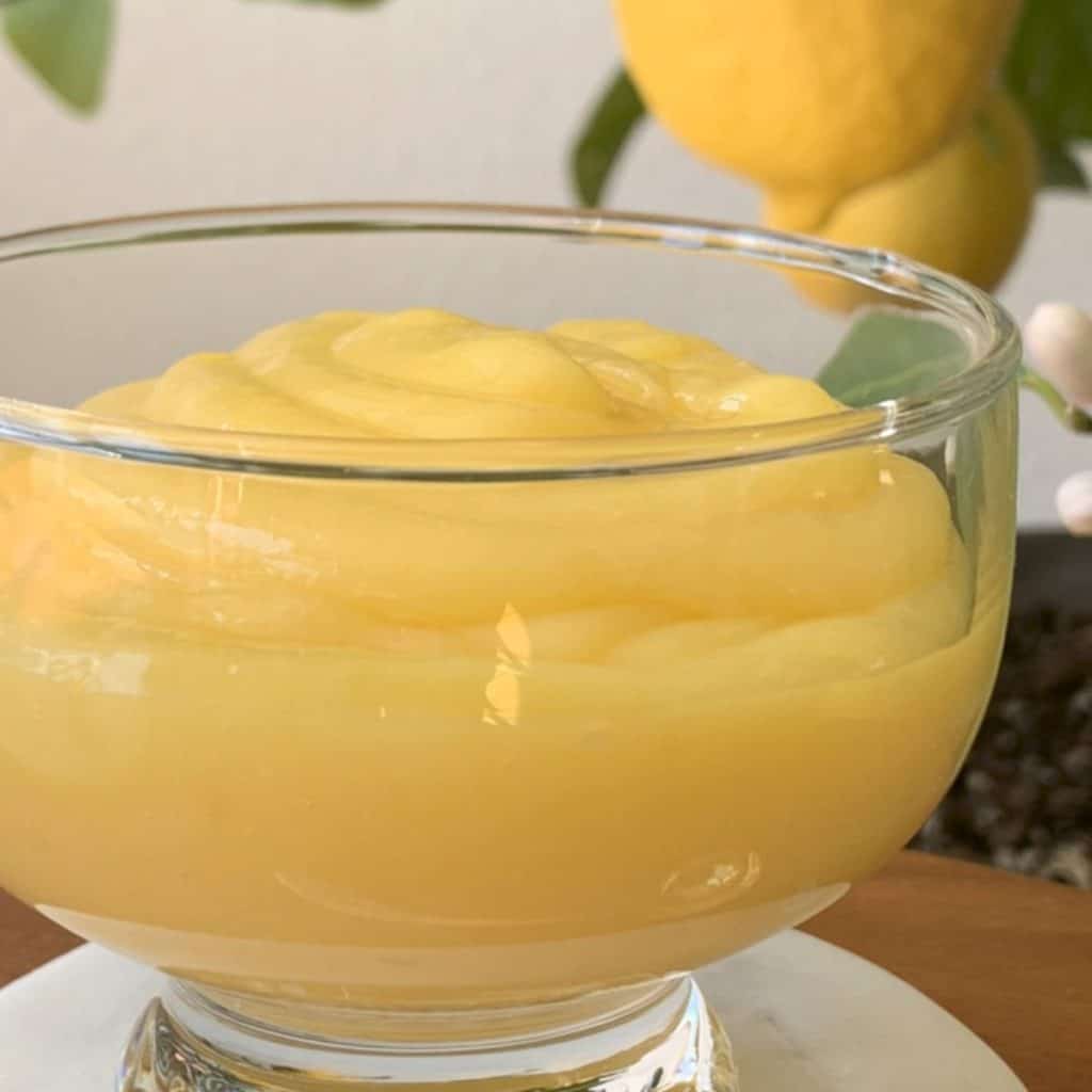 Lemon curd in a glass bawl and a lemon in a background.