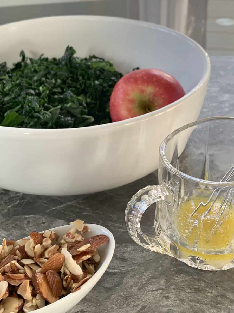 Shredded kale and an apple in the white ball and almond praline and dressing in the foreground.