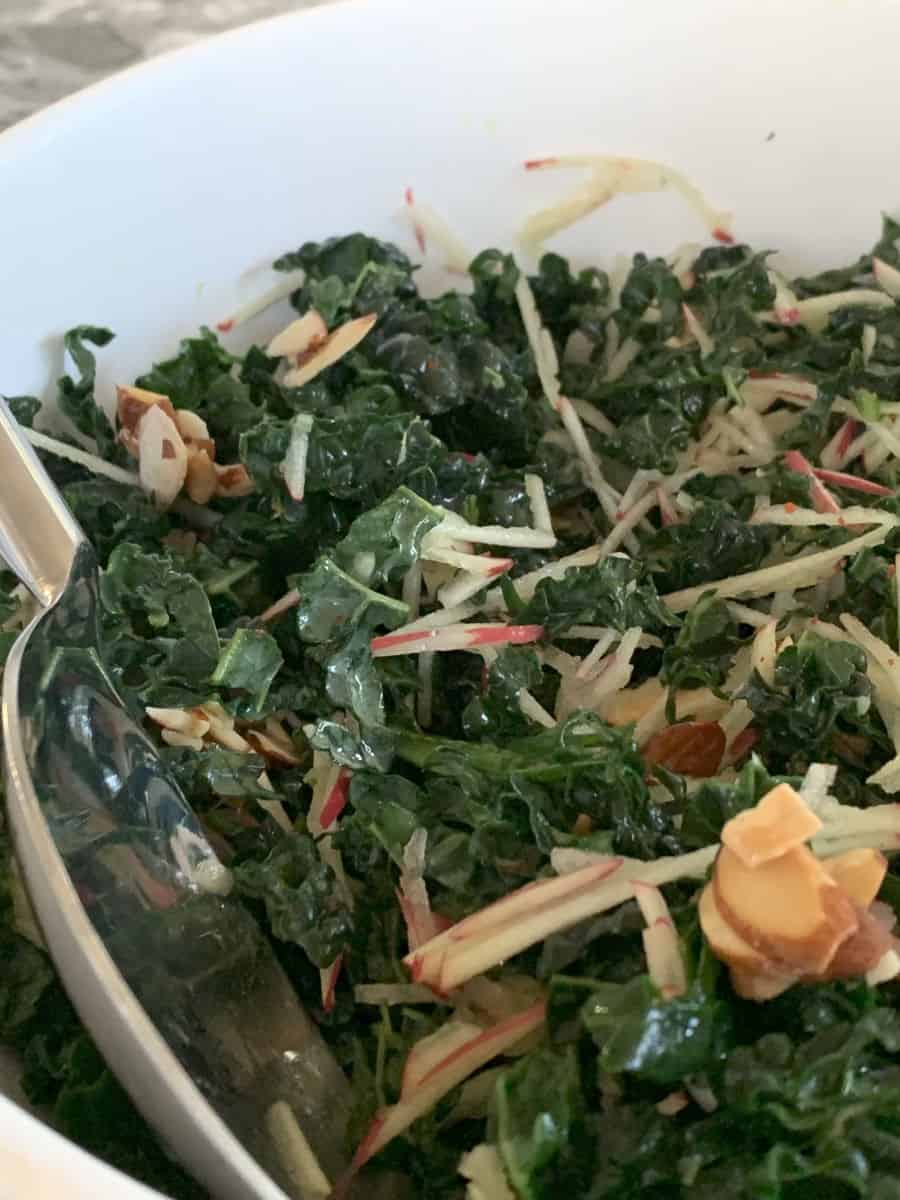 Kale and apple salad in a bowl with a serving spoon.