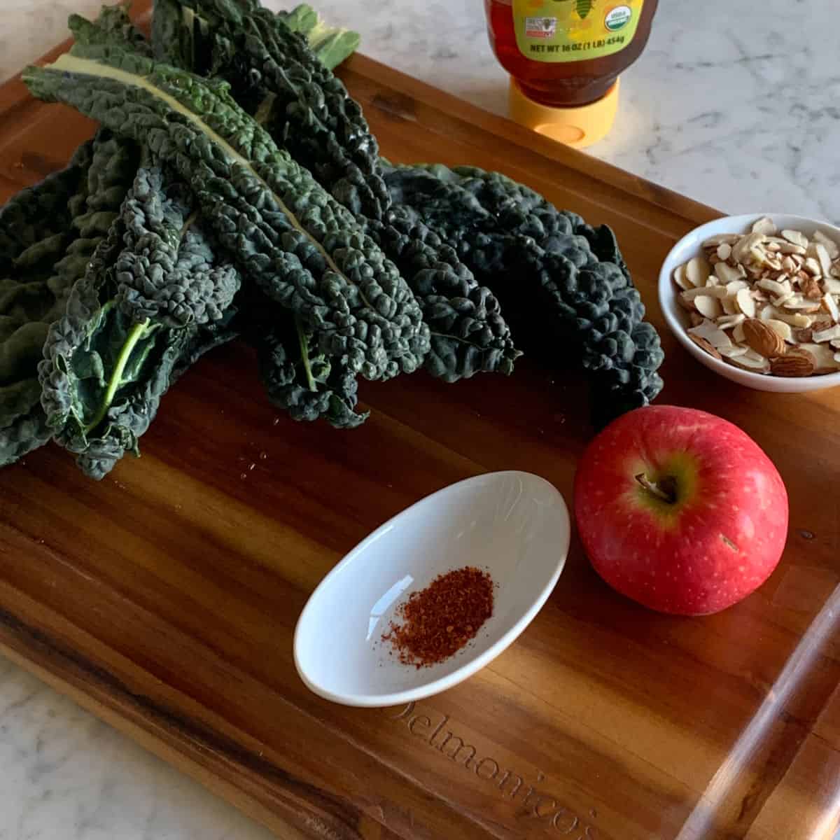 Kale, apple, almonds and chili peppers on the cutting board and honey in the background.