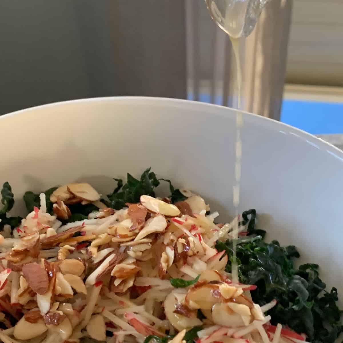 Dressing is being poured over the kale, shredded apples, and almond praline.