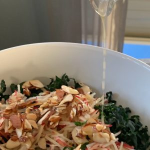 Pouring dressing on the kale and apple salad.