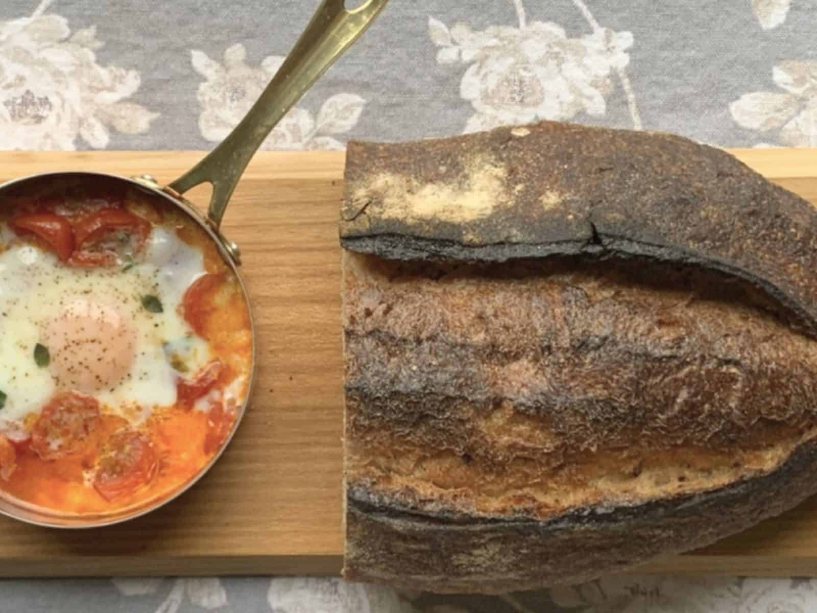 The shirred eggs and a loaf of bread on a cutting board.