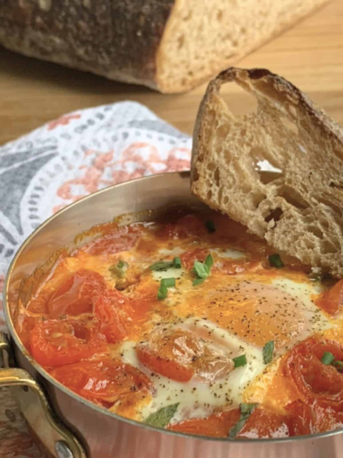 The shirred eggs and tomato confit in a small copper pan with a crusty bread.