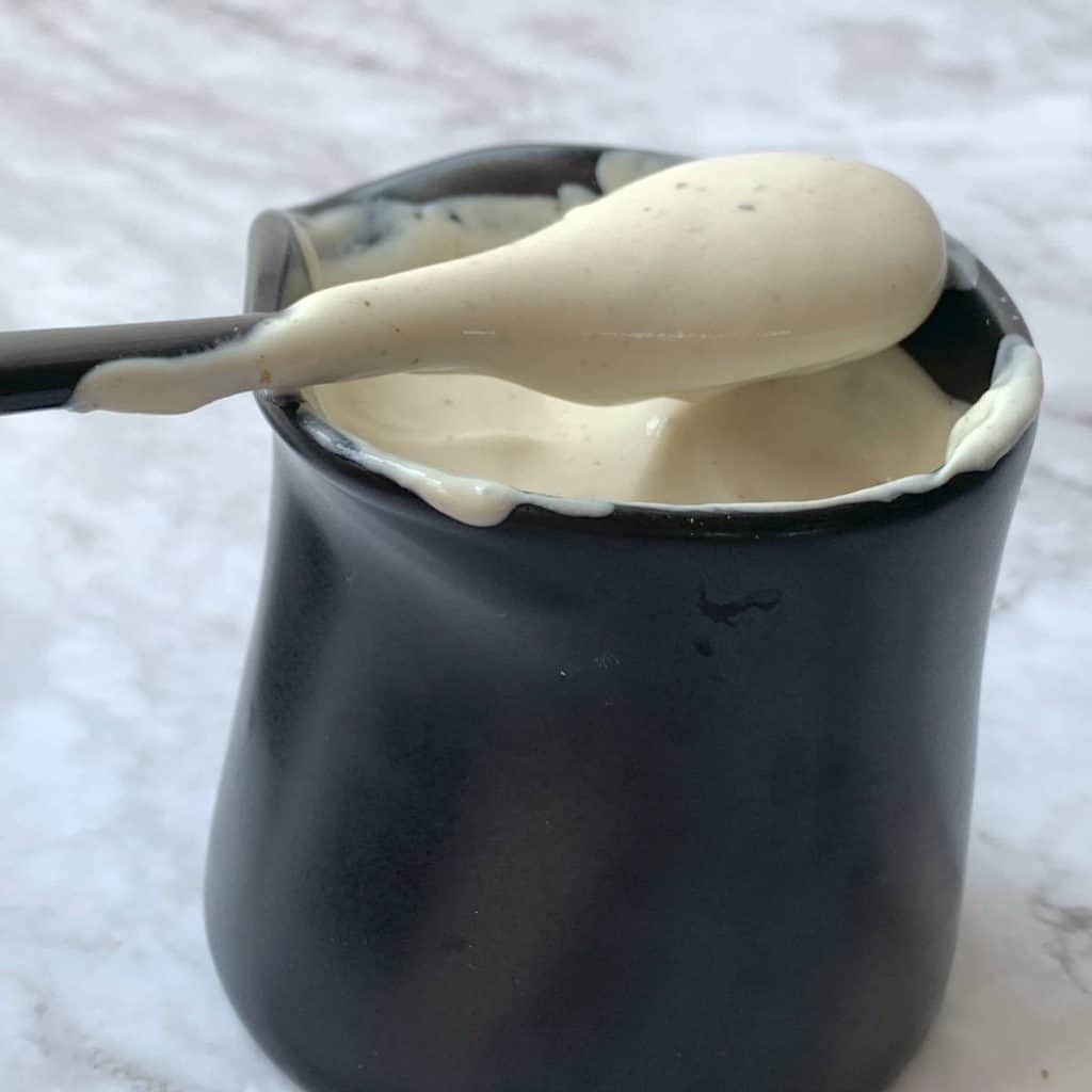 A spoon in a cup of white sour cream dressing.