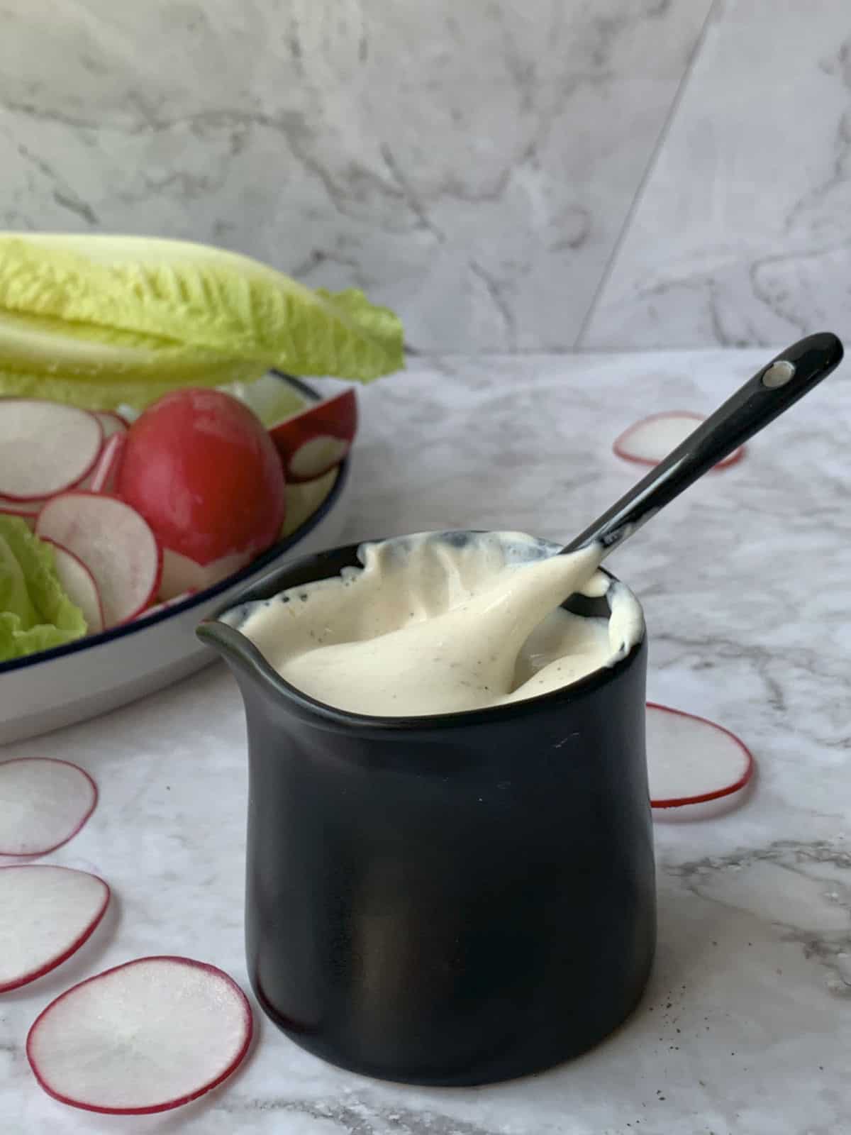 Jar of sour cream dressing with green salad in a background.