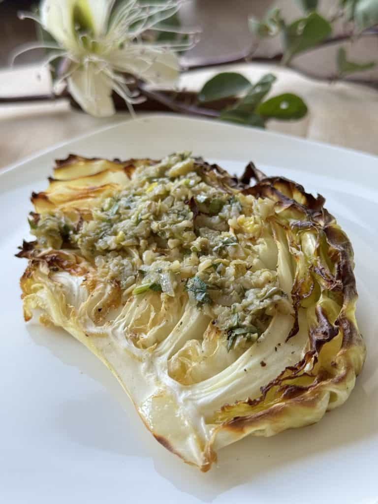 Charred cabbage with caper tarragon tapenade on a white plate.