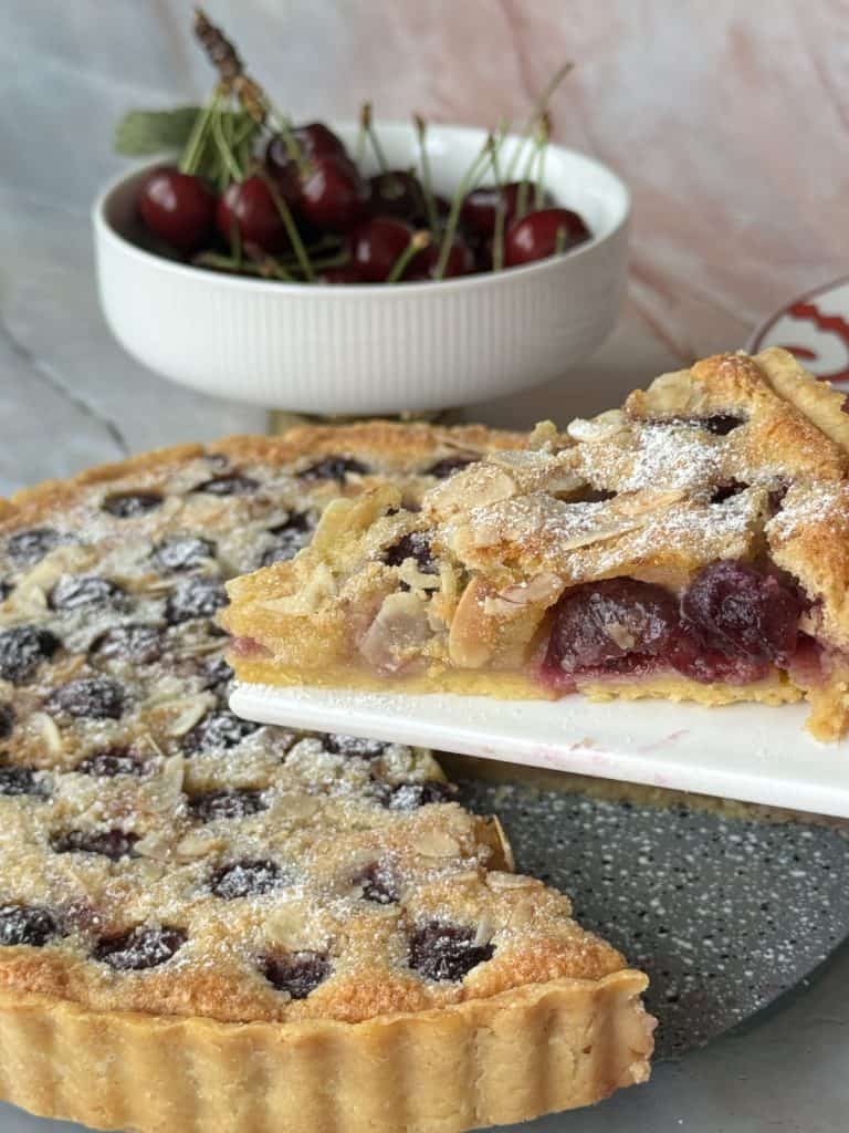 Cherry tart in a foreground and bowl of cherries in a background.