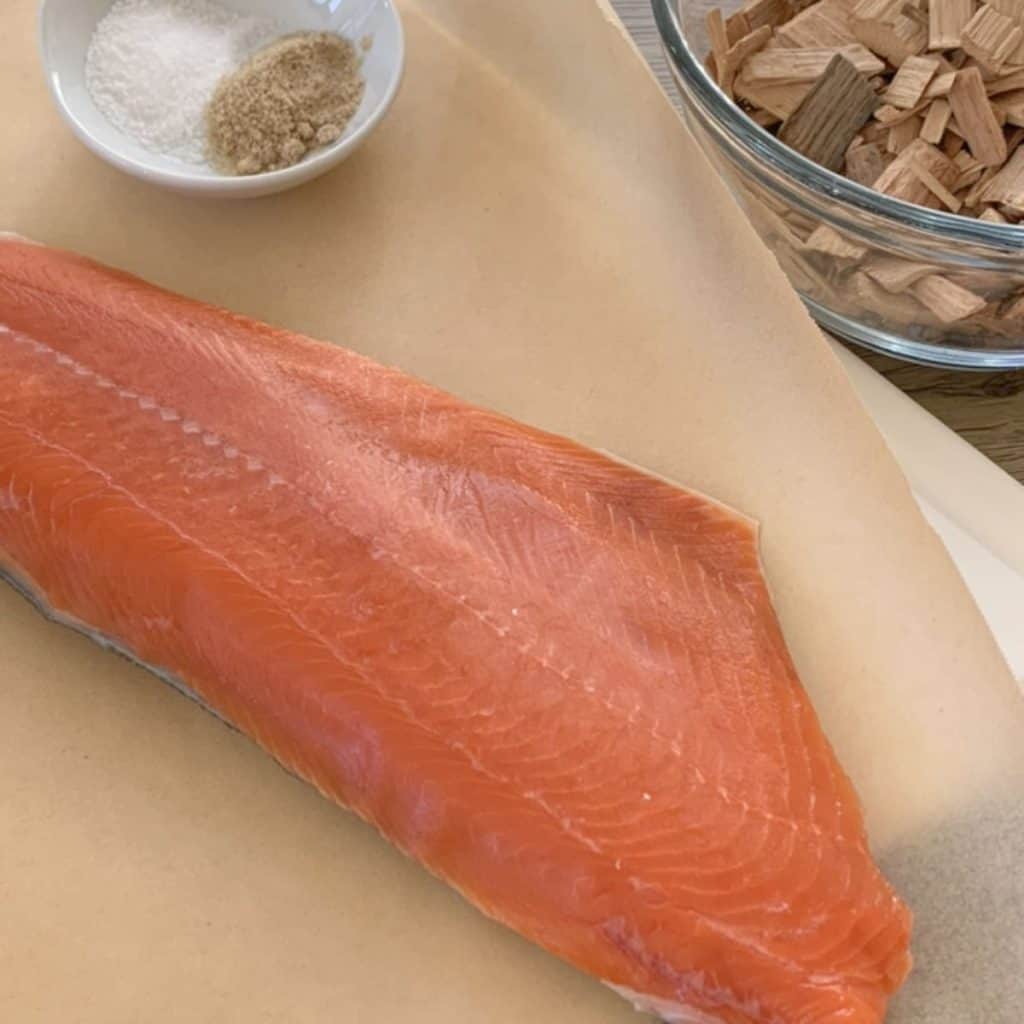 Salmon on a parchment paper and wood chips on the glass bowl.