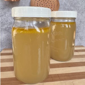 Two jars of beef bone broth on a board.