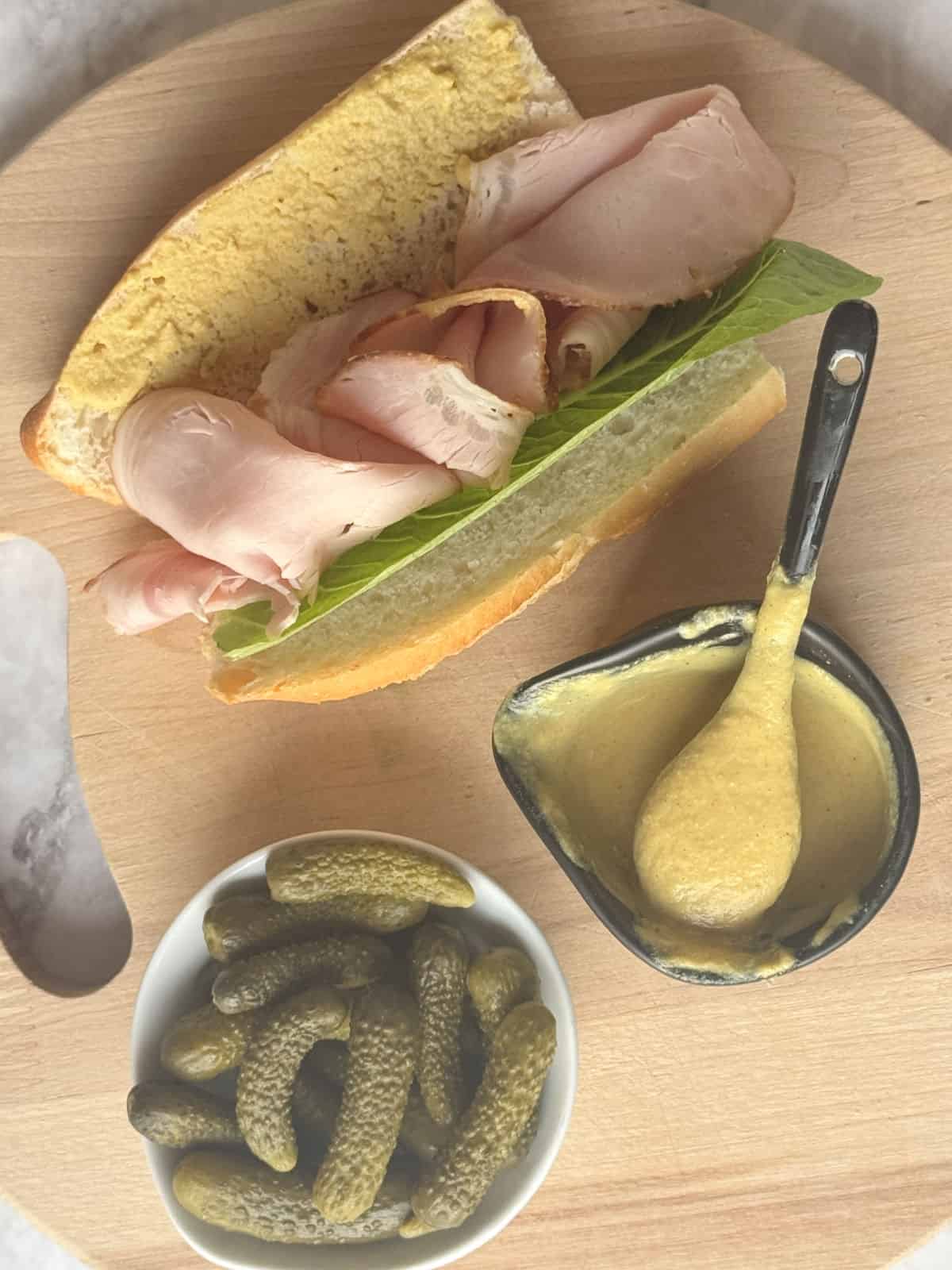 Jar of mustard with a ham sandwich.