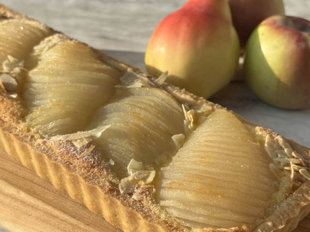 Pear tart in a foreground and fresh pears in a background.