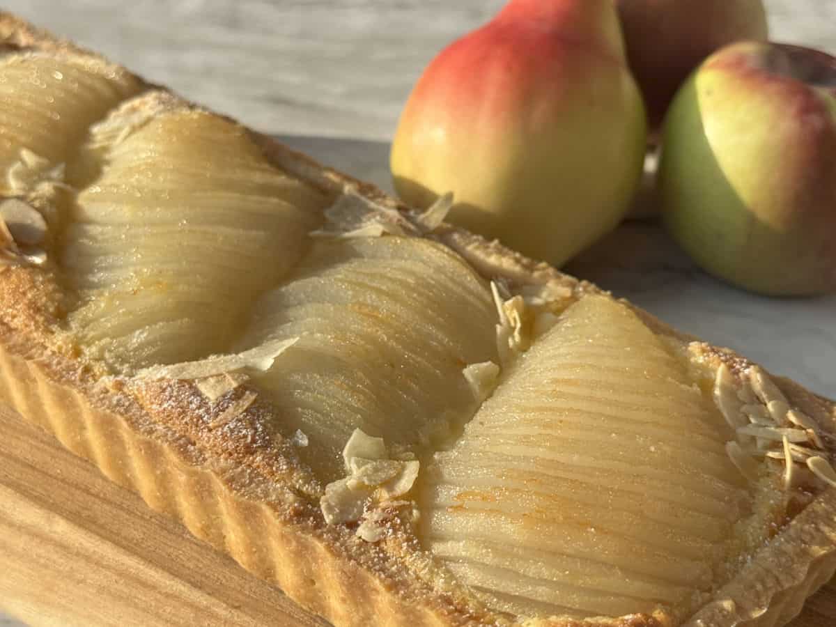 Pear tart in a foreground and fresh pears in a background.