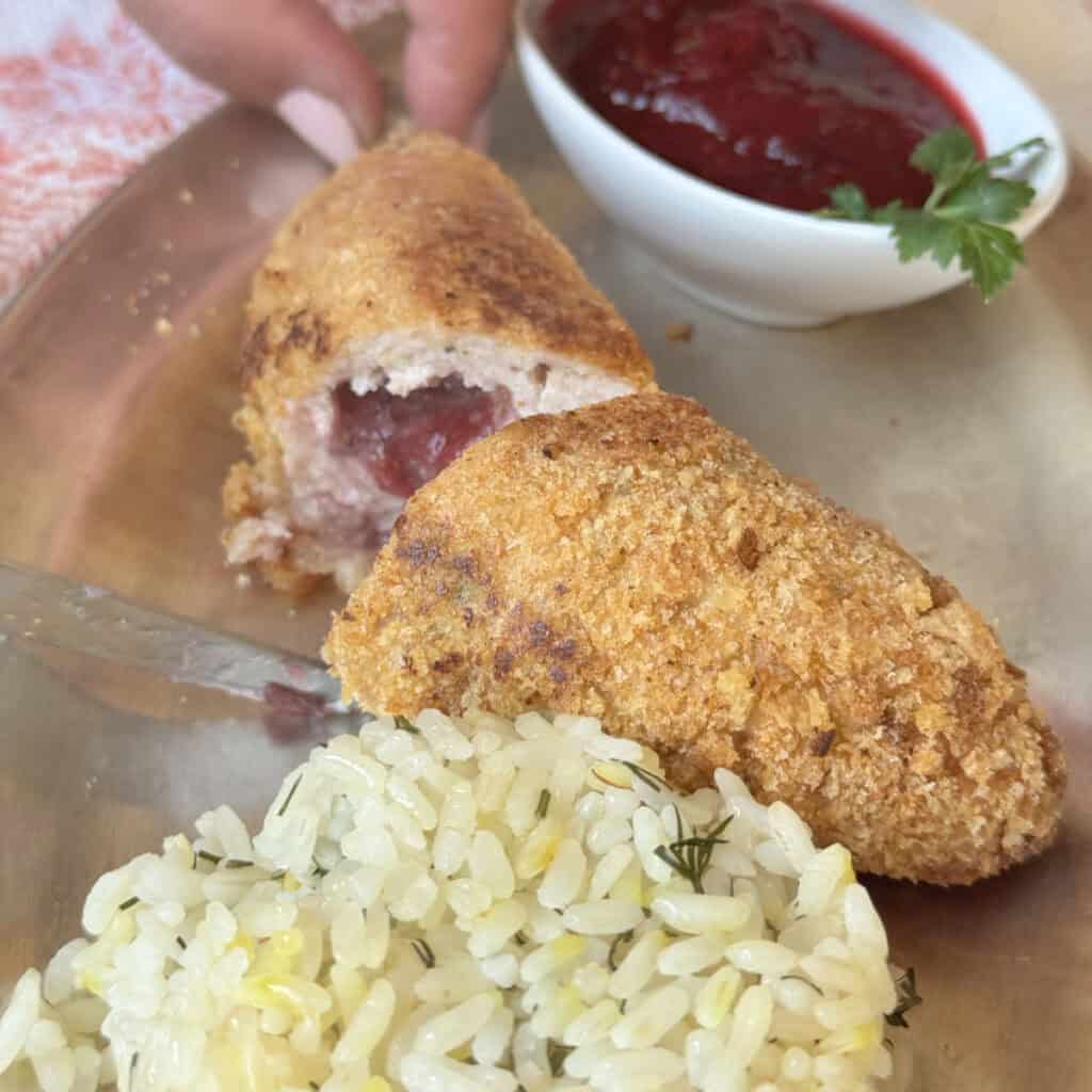 Chicken Kiev kotlet cross-cut with a bed of rice and cranberry sauce.