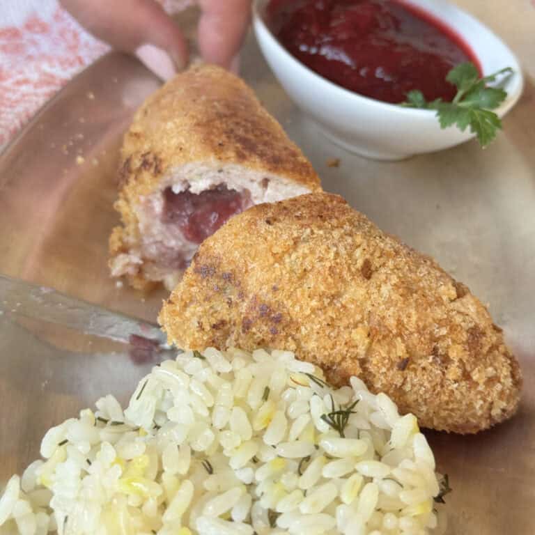 Chicken Kiev kotlet cross-cut with a bed of rice and cranberry sauce.