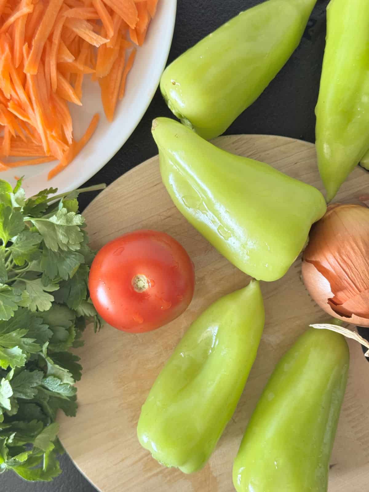 A close-up of fresh ingredients used in stuffed pepper, including peppers, shredded carrots, tomatoes and onion.