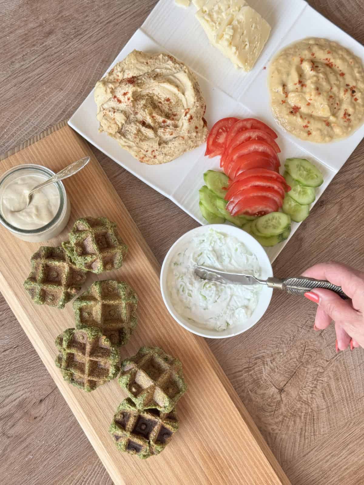 An overhead shot of a beautifully spread of meze with falafel waffles arranged on a wooden board.
