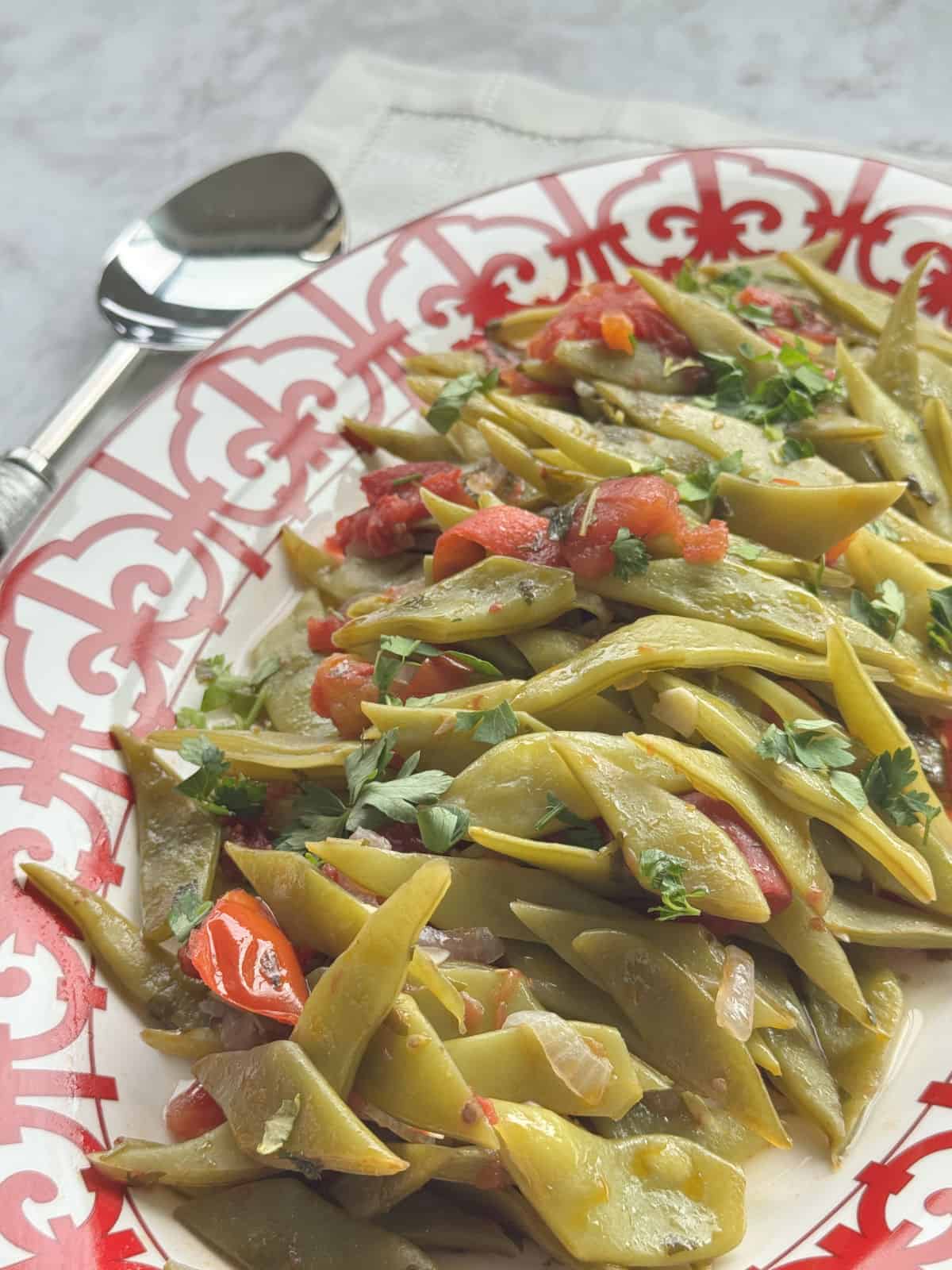 Green beans with tomatoes and onions on a red platter.