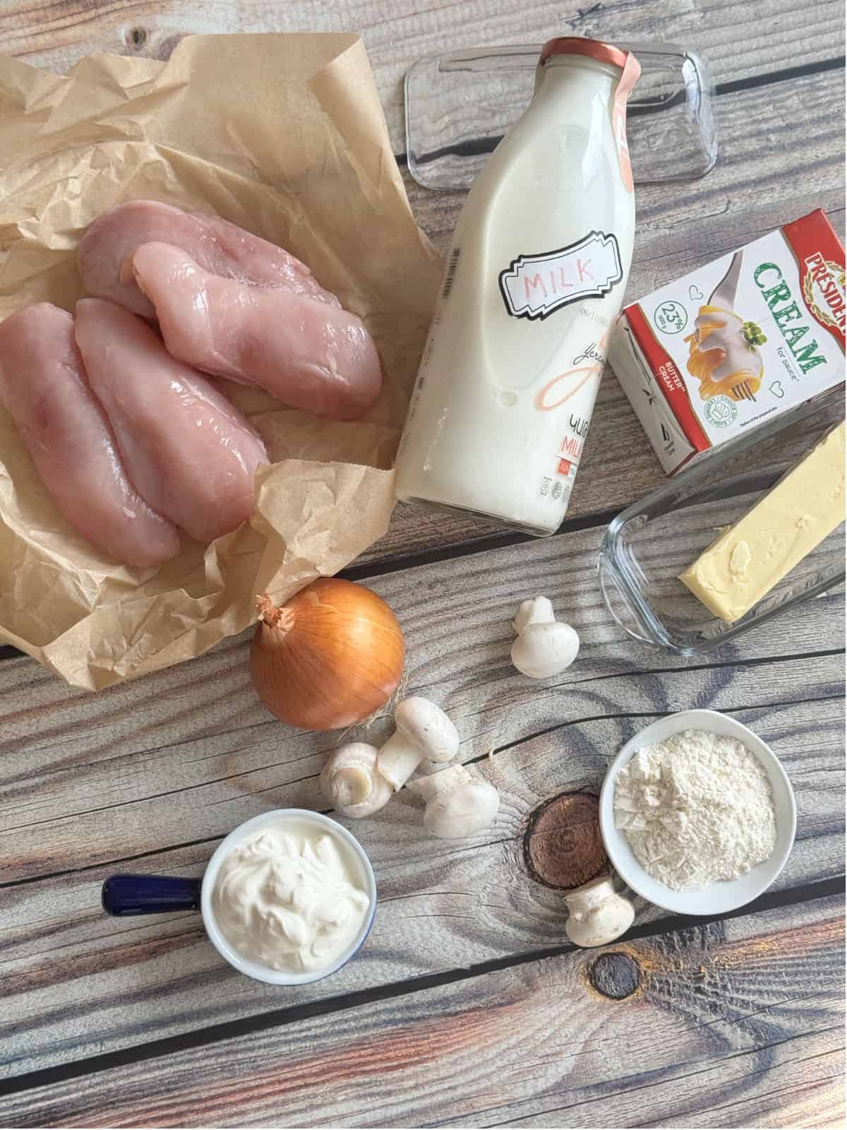 A close-up of fresh ingredients used in Chicken Julienne, including chicken breast, onion, milk, cream, and mushrooms.