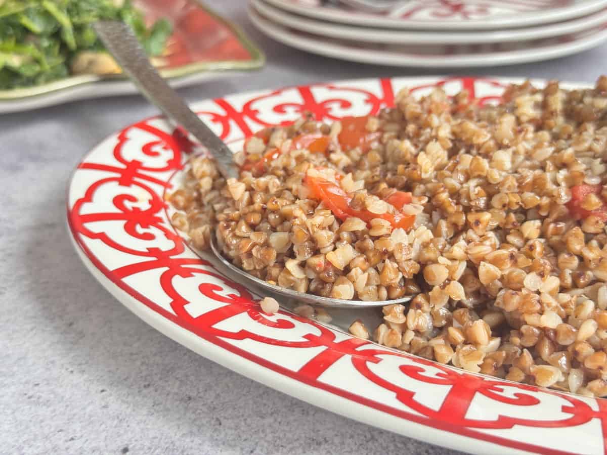 Buckwheat pilaf on a red plate with a spoon.