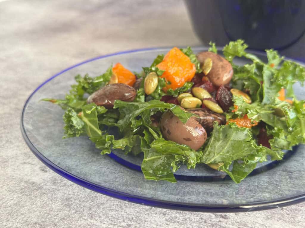 Roasted butternut squash salad with gigante beans, beets, and kale on a blue plate.