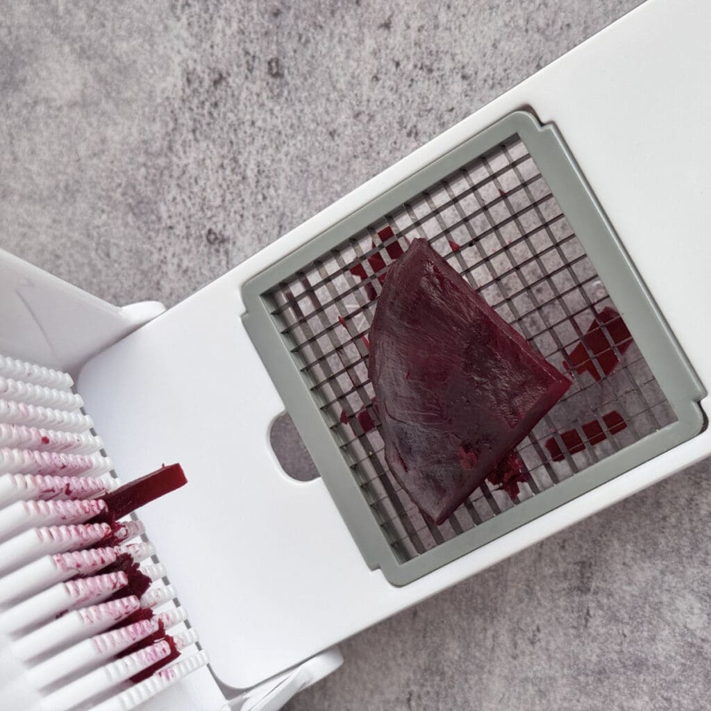 Cutting cooked beets into even cubes with a vegetable chopper.