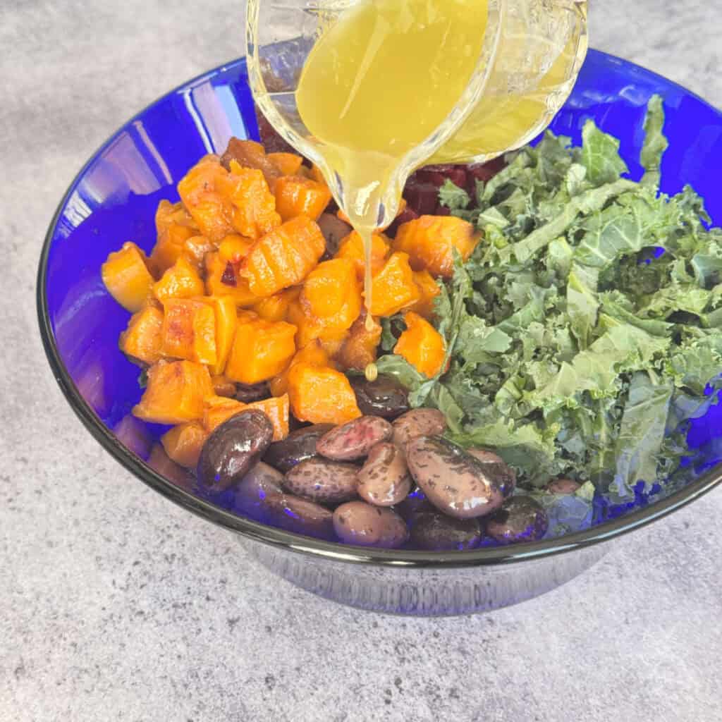 Pouring white balsamic dressing over the kale, beans, squash, and beets.