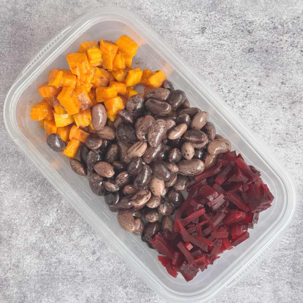 Precooked butternut squash, beets, and gigante beans stored in a container for make-ahead assembly.